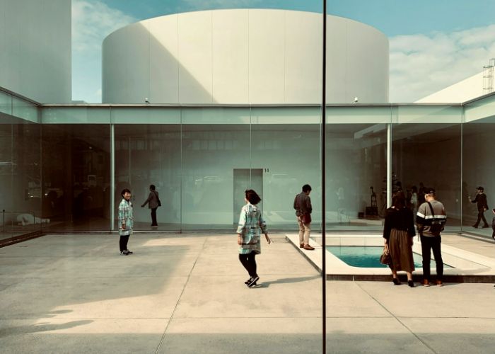 A photo taken through a window at Kanazawa's 21st Century Museum of Contemporary Art, showing people looking at exhibits.